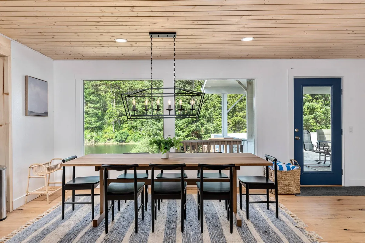 A warm and welcoming dining area featuring a large table, an elegant chandelier, and expansive windows with a view of the outdoors. The space is set for family dinners, social gatherings, and game nights, with natural light and outdoor vistas enhancing the ambiance.