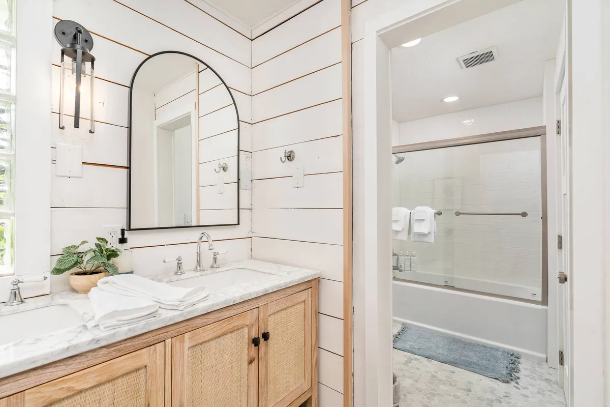 A serene and modern bathroom with a double sink, large mirror, wooden cabinetry, and a separate shower area. The room is filled with natural light, creating a relaxing atmosphere for morning and evening routines.