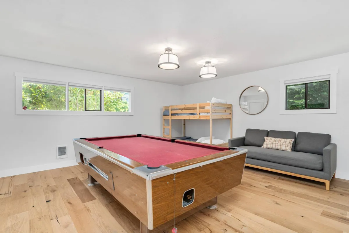 A spacious, multifunctional game and sleeping room featuring a pool table, comfortable sofa, bunk bed, and large windows. The space is designed for both recreation and rest, offering an area where guests can unwind, play games, or sleep.