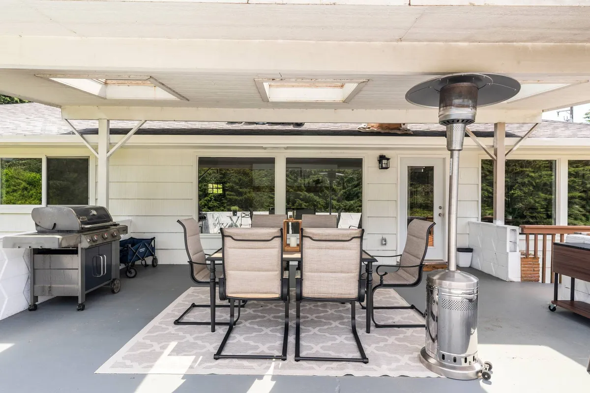 This exterior image shows a spacious patio area with an outdoor dining table, grill, and patio heater set up for social gatherings. The setting suggests a seamless blend of indoor and outdoor living, perfect for enjoying meals or relaxing with family and pets.