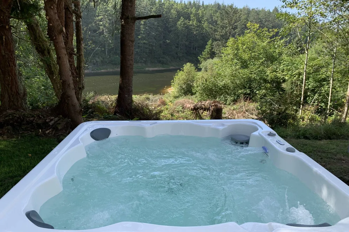 This exterior image shows a lakeside hot tub set within a natural landscape, with calm water visible in the background. The scene is tranquil and inviting, suggesting a place to unwind after a day of water sports or fishing, seamlessly connecting active recreation with relaxation.
